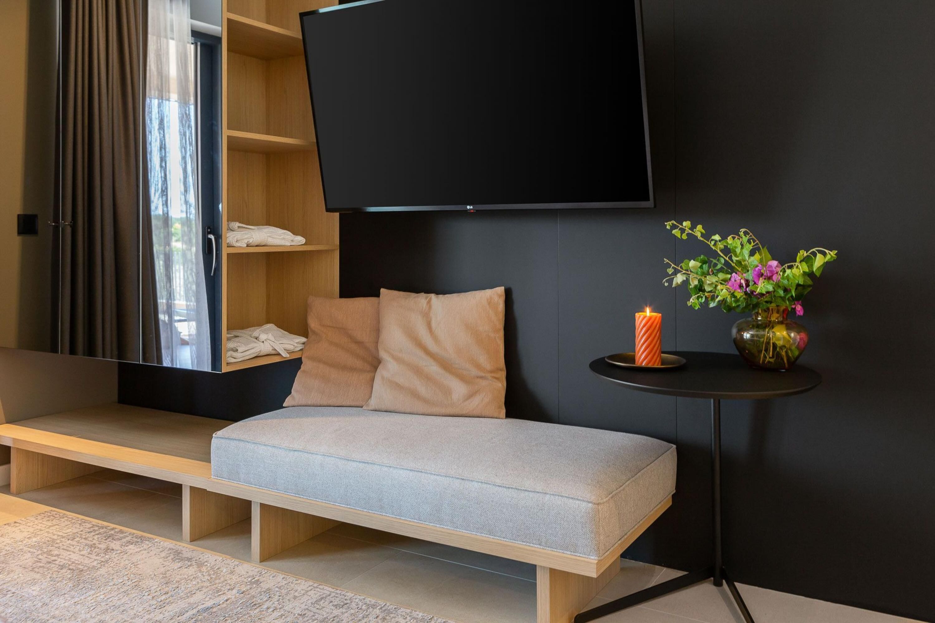Un salon moderne avec un canapé, un téléviseur à écran plat, une petite table ornée d’une bougie et de fleurs, et un banc en bois.