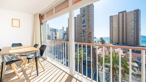 A balcony with a wooden floor, a table with chairs, and a view of tall buildings and a body of water. - Edimar 7-6 Apartment Levante Beach (Benidorm)