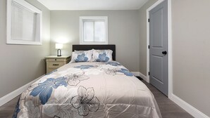 A bedroom with a bed, nightstand, and two windows.