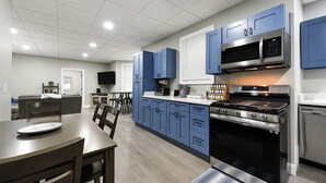 A modern kitchen with blue cabinets, a stainless steel stove, and a flat-screen TV mounted above the counter.