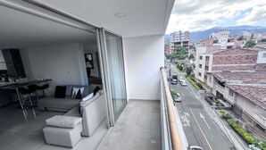 Een modern balkon met een bank en eethoek, met uitzicht op een straat met gebouwen en een berg in de verte.