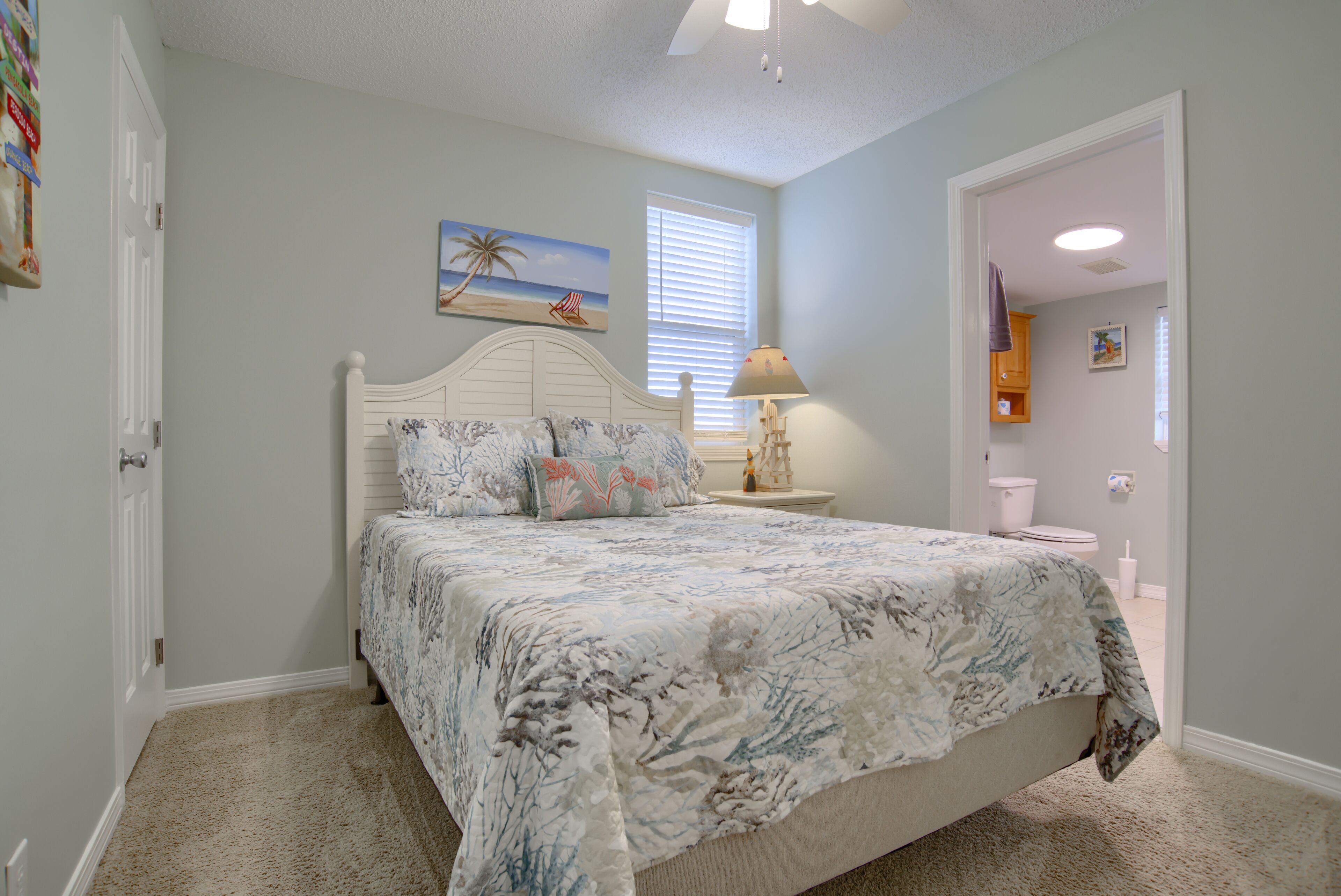 A bedroom with a bed, a nightstand, a lamp, a painting, and a window with blinds.