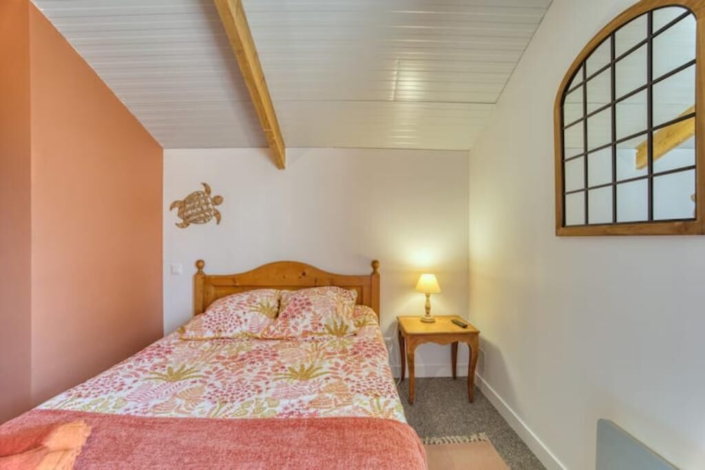 Ein Schlafzimmer mit einem hölzernen Bett, einem Nachttisch mit Lampe und einem Fenster mit Gittermuster.