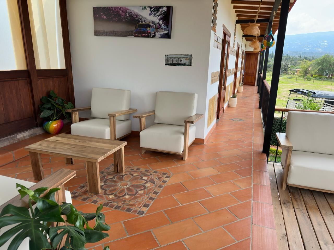Un área de estar al aire libre techada con dos sofás blancos, una mesa de madera y plantas en macetas.