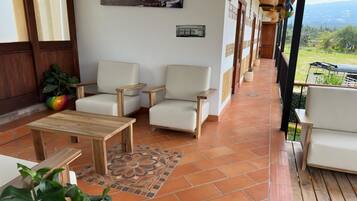 Un área de estar al aire libre techada con dos sofás blancos, una mesa de madera y plantas en macetas.