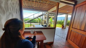 Una mujer sentada a una mesa junto a una ventana con vista a una escalera y follaje exterior.