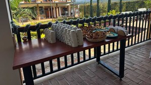 Un balcón con una mesa dispuesta para el desayuno, con vistas a una casa y un paisaje montañoso.