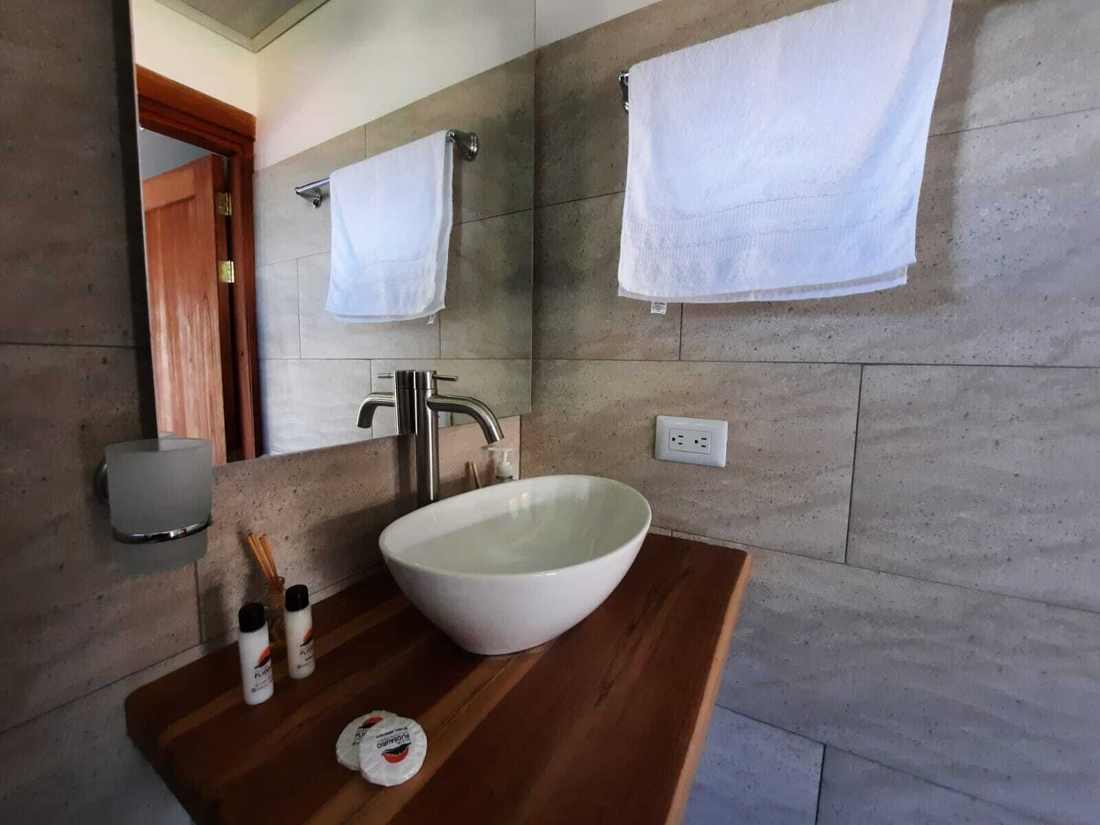 Ein Badezimmer mit einem großen weißen Waschbecken, einem Spiegel und zwei weißen Handtüchern, die an der Wand hängen.