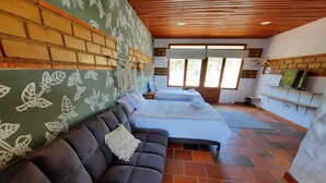 Una habitación con sofá de cuero oscuro, cama con ropa de cama blanca, pared de ladrillo con motivos florales y techo de madera.