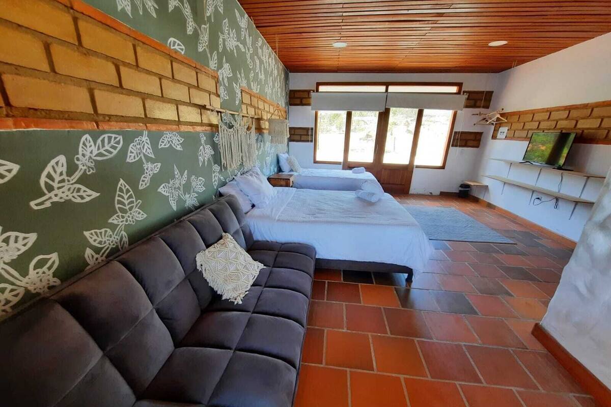 Une pièce avec un canapé en cuir foncé, un lit avec une literie blanche, un mur en briques orné de motifs floraux et un plafond en bois.