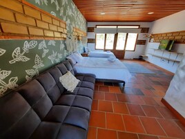 Una habitación con sofá de cuero oscuro, cama con ropa de cama blanca, pared de ladrillo con motivos florales y techo de madera.