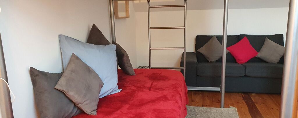 Ein Zimmer mit einem Bett, einer Schlafcouch und einer Metallleiter.