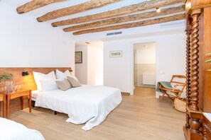 Una camera da letto con soffitto in legno, un letto con biancheria bianca, un comodino con una lampada e una sedia.