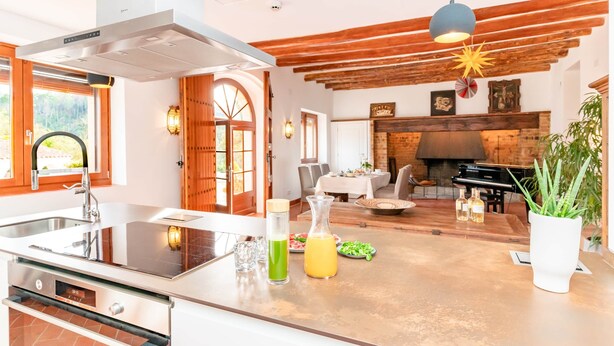 A modern kitchen with a large island, a dining area with a fireplace, and a living room with wooden beams.