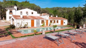 A white villa with a swimming pool, outdoor seating, and a forested backdrop.