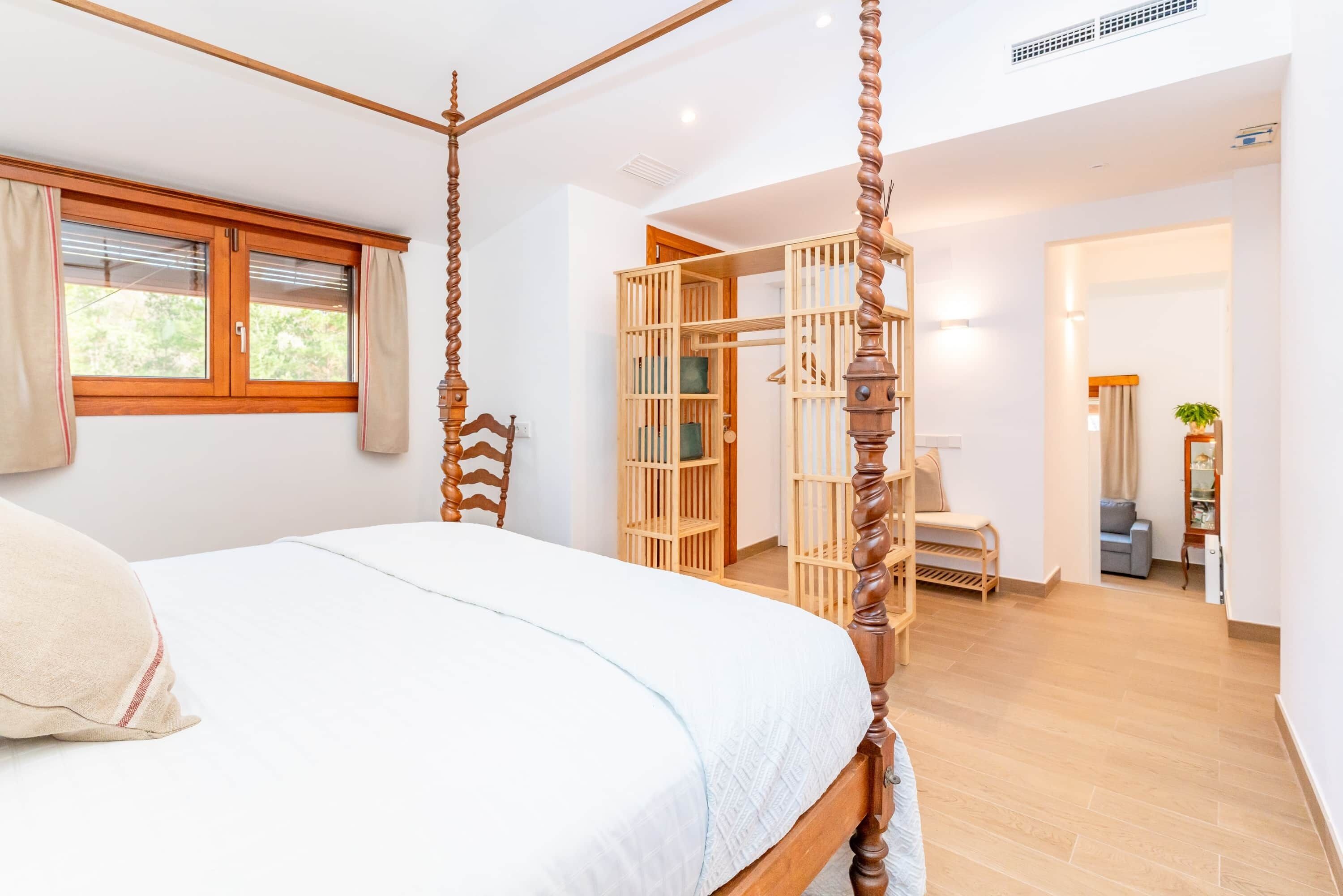 A bedroom with a four-poster bed, a wooden wardrobe, and a small seating area with a chair.