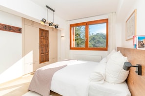 Une chambre à coucher avec un lit, une fenêtre donnant sur un paysage verdoyant, une armoire en bois et une lampe fixée au mur.
