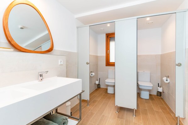 Une salle de bain moderne avec un lavabo blanc, un grand miroir ovale et deux toilettes.