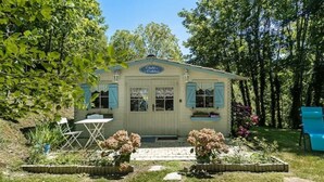 A small, single-story building with a sign reading "Chalet de la Forêt." It features a front door, windows, and a small patio area with a table and chairs.