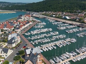 An aerial view of a marina with numerous boats docked, surrounded by residential buildings and a hilly landscape in the background.