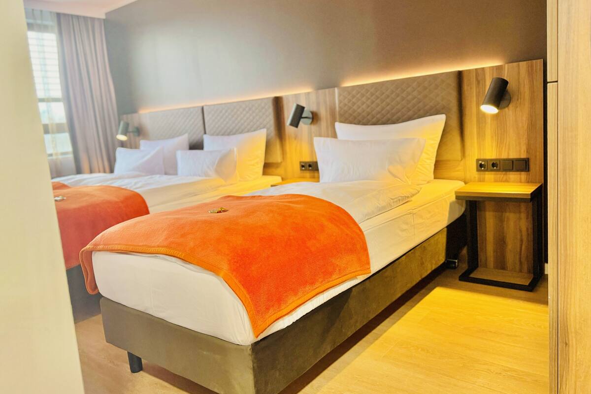 Ein modernes Hotelzimmer mit einem großen Bett, zwei Nachttischen und einem Kopfteil mit integrierter Beleuchtung.