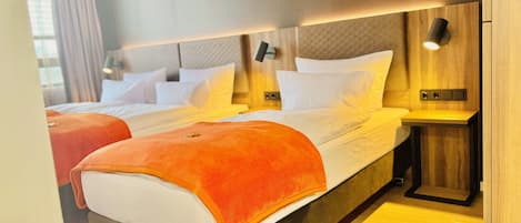 Una habitación de hotel moderna con una cama grande, dos mesitas de noche y un cabecero con iluminación integrada.