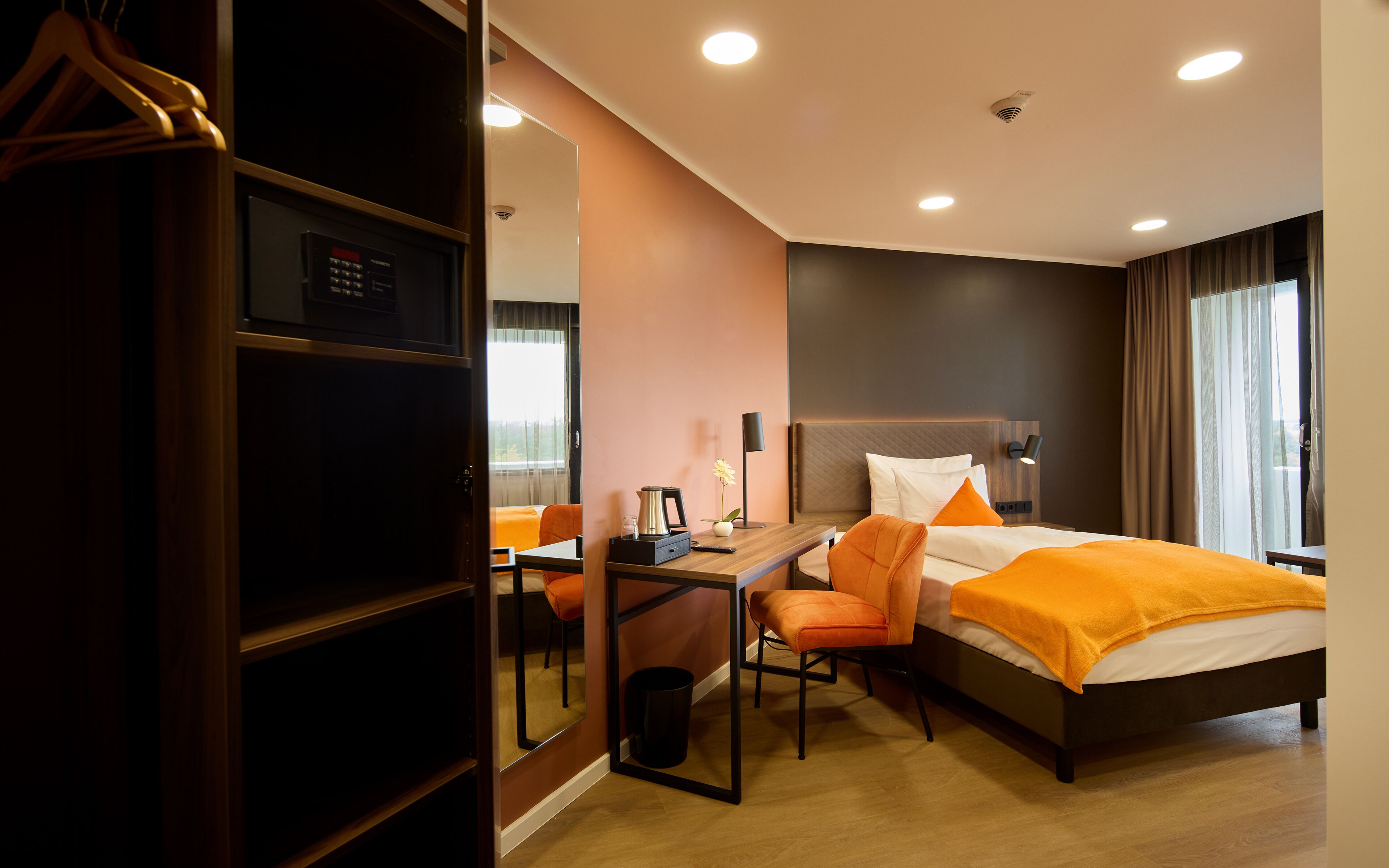 A hotel room with a bed, a desk, a chair, and a wardrobe.