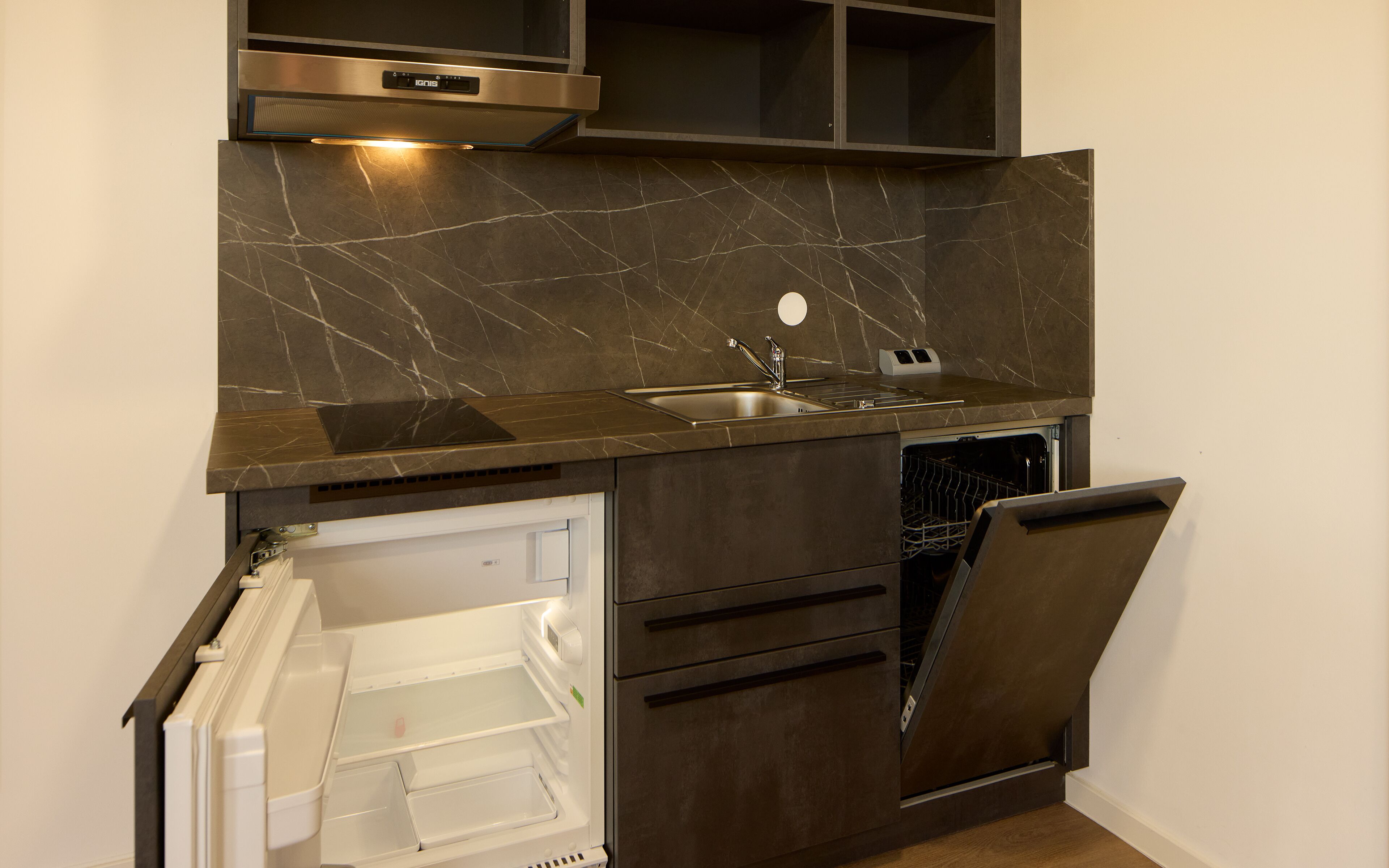 A compact kitchen with a built-in dishwasher, a stainless steel sink, and dark cabinetry.
