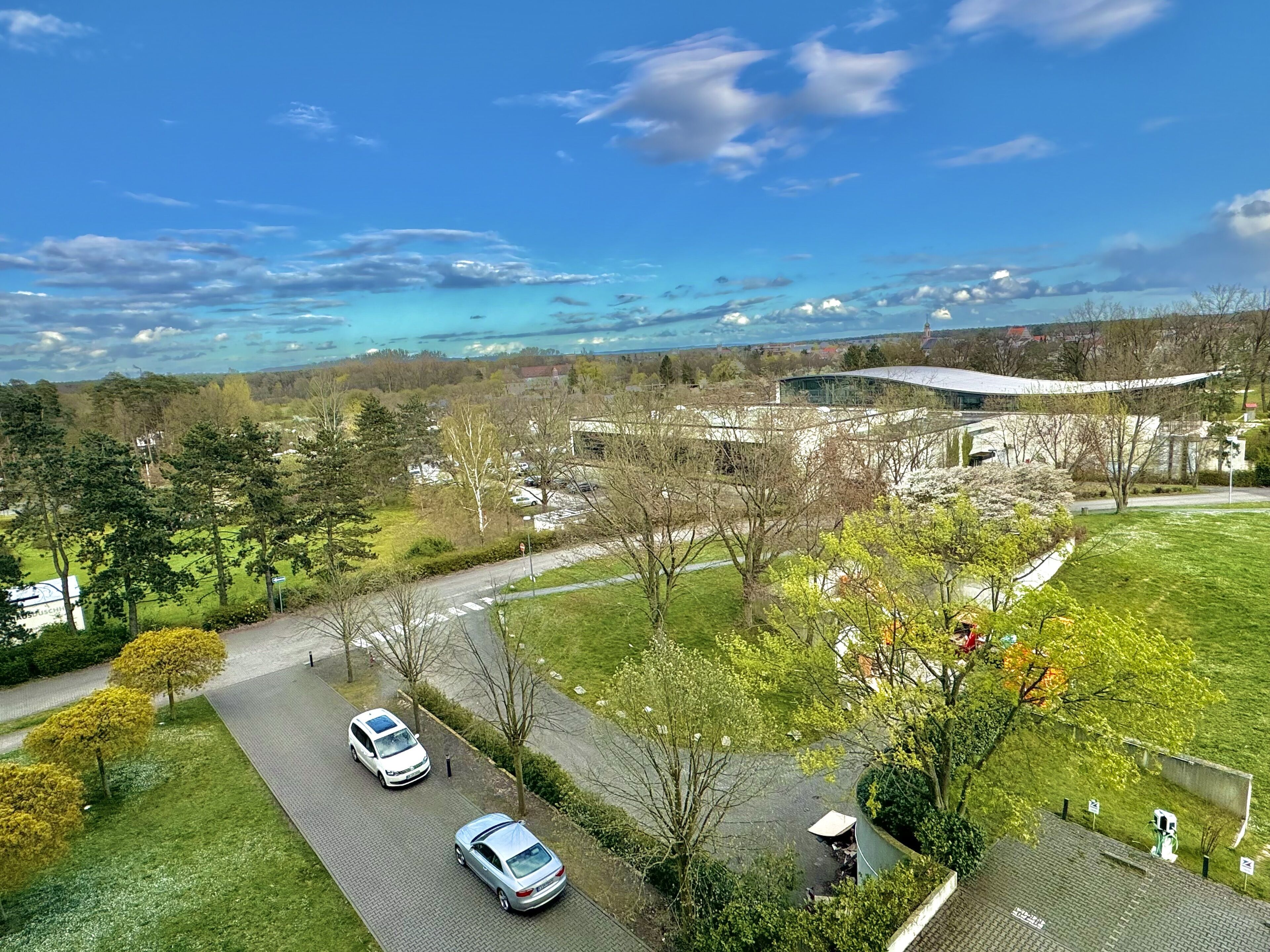 A residential area with two parked cars, a green lawn, and a modern building with a curved roof.