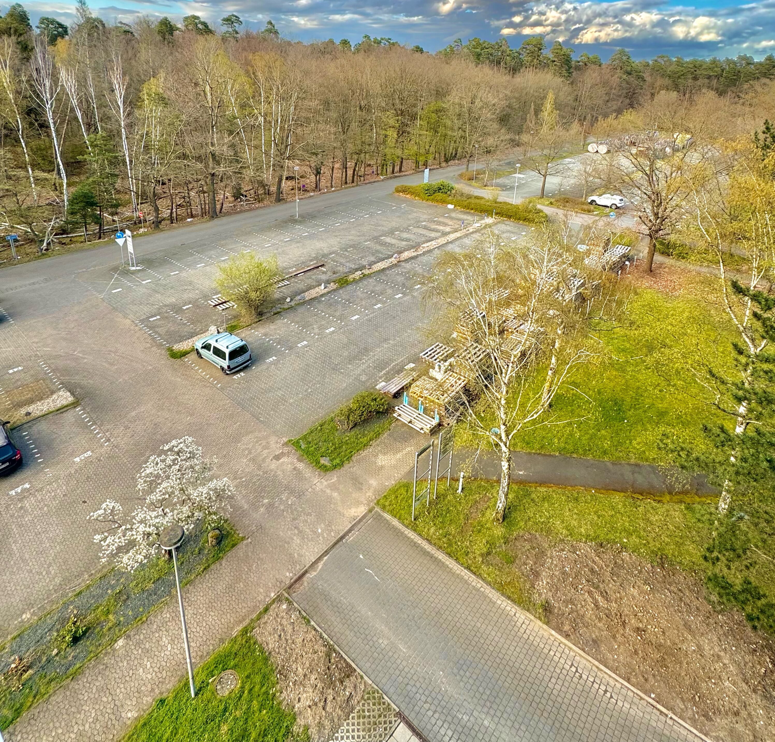 Luchtbeeld van een parkeerplaats met enkele auto's, omringd door bomen en groen.
