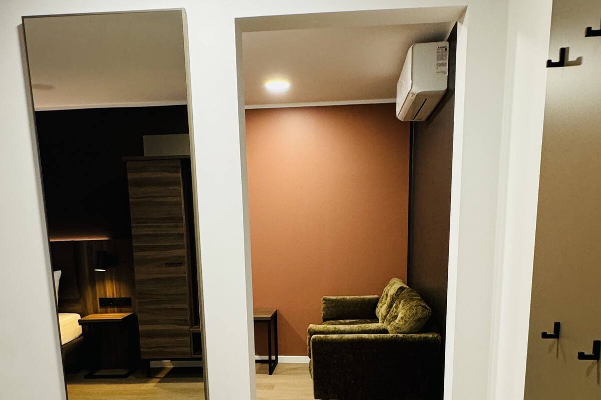 Ein Zimmer mit Holzboden, einem Sofa, einer Lampe und einem Spiegel, der einen Teil des Raumes reflektiert.