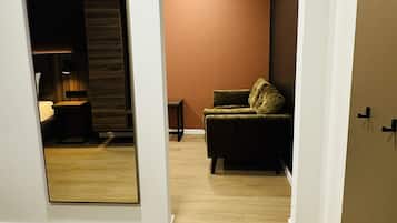 A room with a wooden floor, a sofa, a lamp, and a mirror reflecting part of the room.