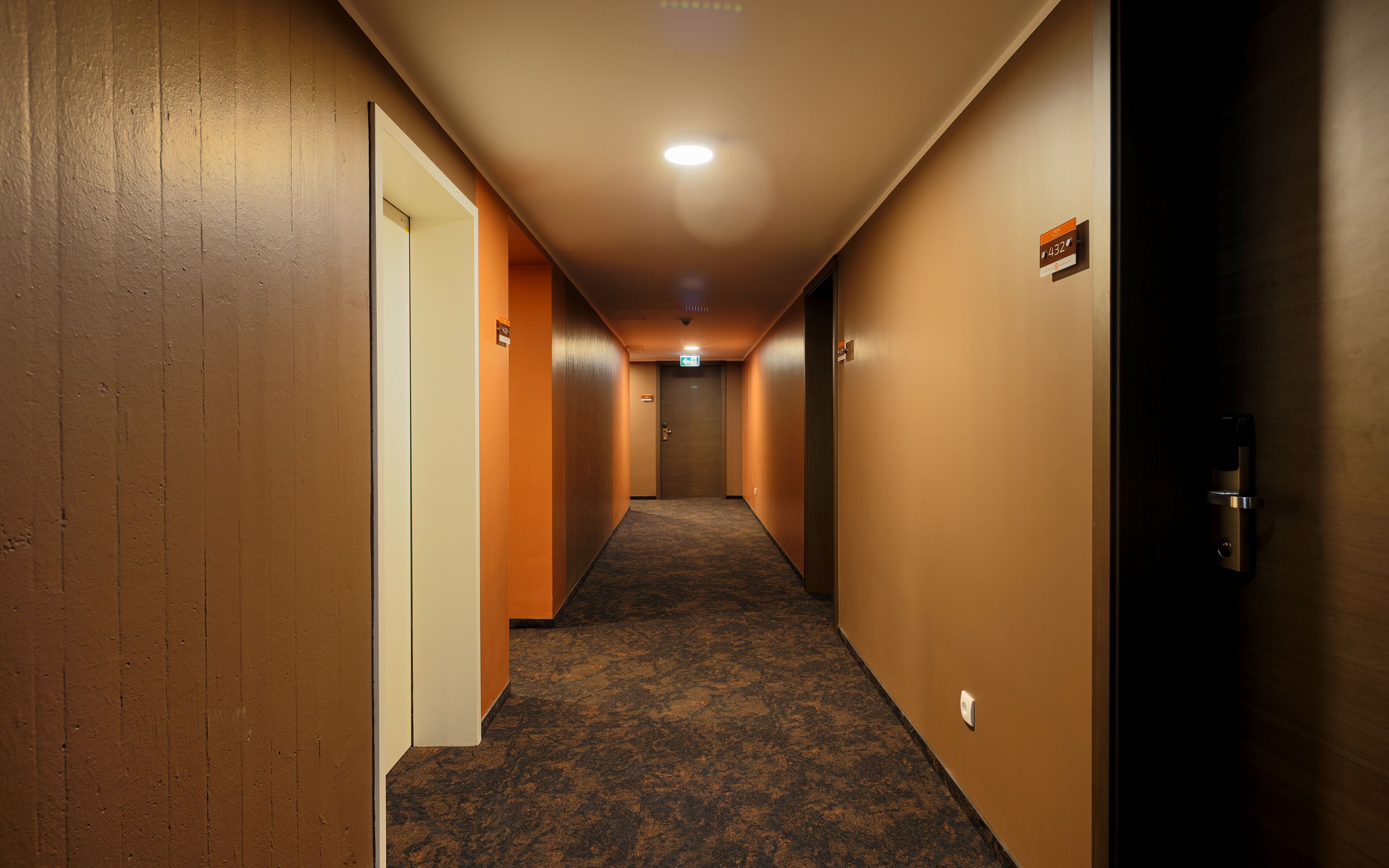 A hotel hallway with carpeted floors, wooden walls, and doors on both sides.
