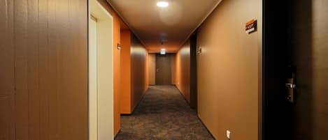 Un pasillo de hotel con pisos alfombrados, paredes de madera y puertas a ambos lados.
