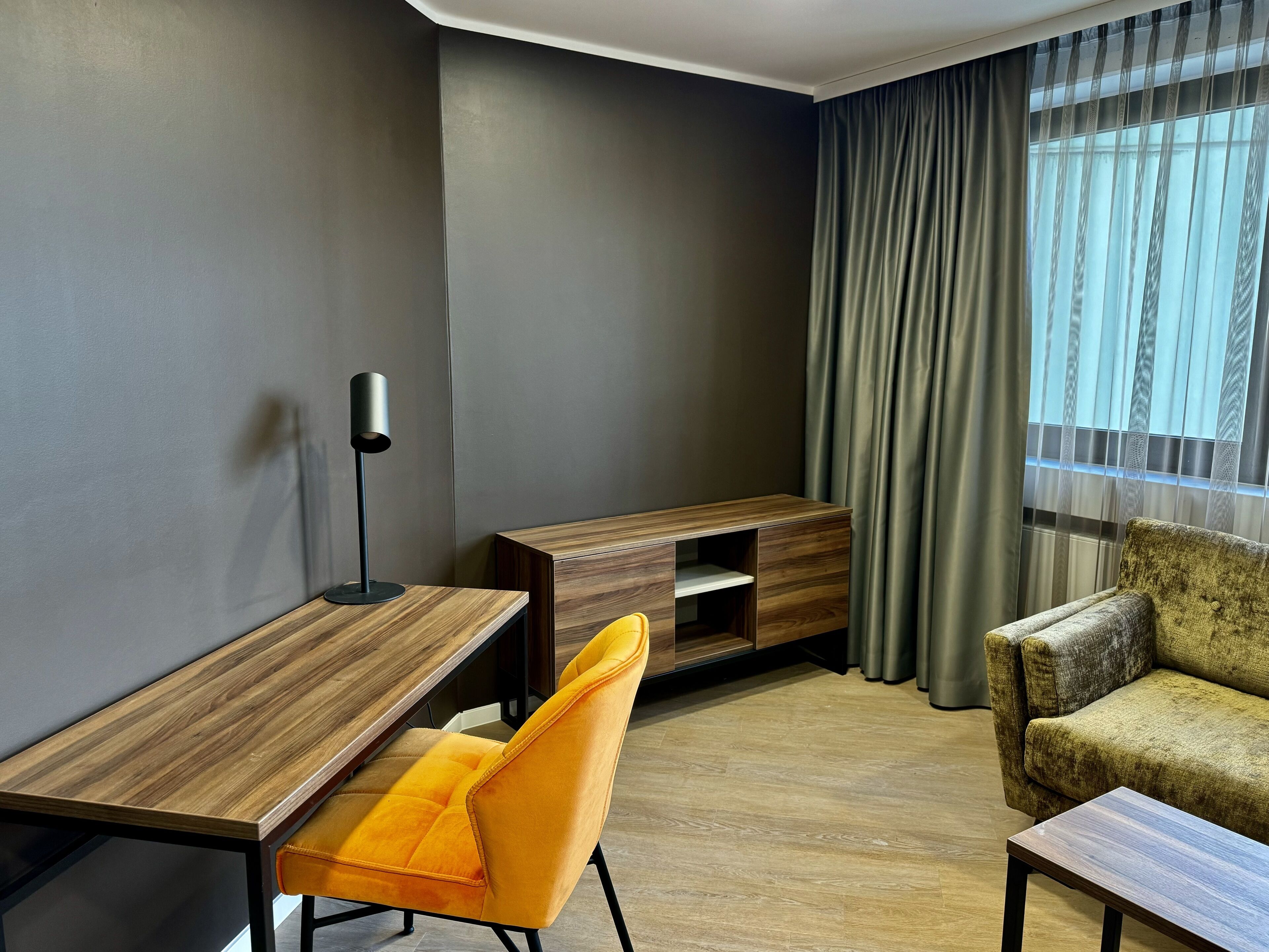A modern room with a wooden desk, a yellow chair, a sofa, and a TV stand.