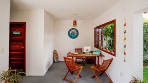 A small dining area with a wooden table and four chairs, a laptop, and a surfboard leaning against the wall. - Boas Ondas Pousada (Tibau do Sul)