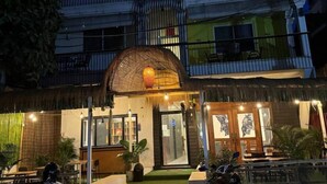 Un bâtiment dont l’entrée est surmontée d’un toit de chaume, avec une porte en verre et une enseigne au-dessus de la porte.