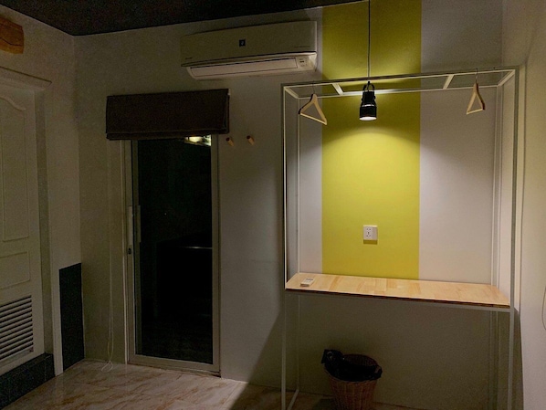 Una habitación con ventana, lámpara colgante y una pequeña estantería de madera.