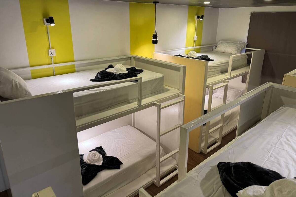 A bunk bed room with multiple beds, each with a mattress and pillows. There are clothes and personal items on the beds.