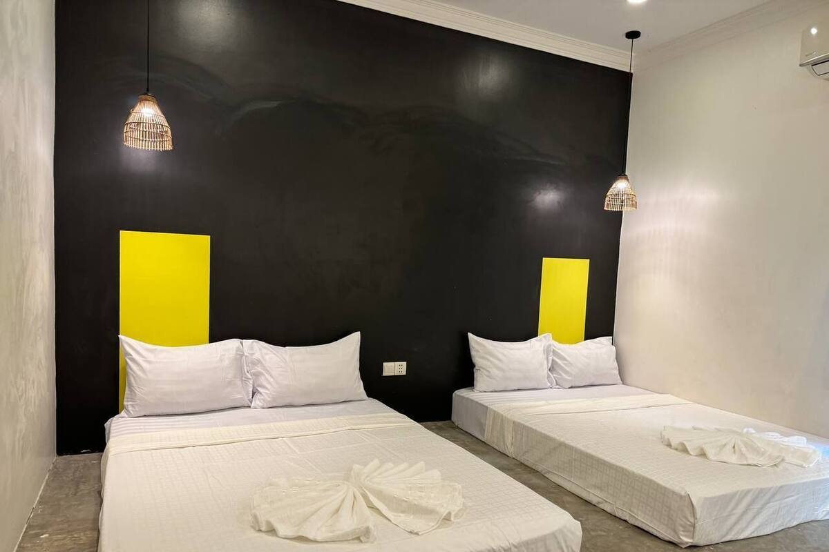 A hotel room with two beds, each with white bedding and pillows, and a large black wall with a yellow accent.