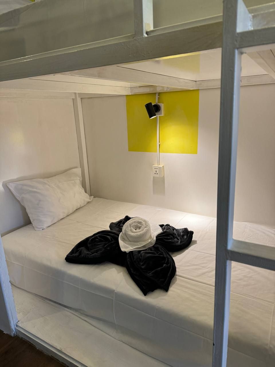 A bunk bed with a white mattress, a black pillow, and a white hat on the lower bunk.