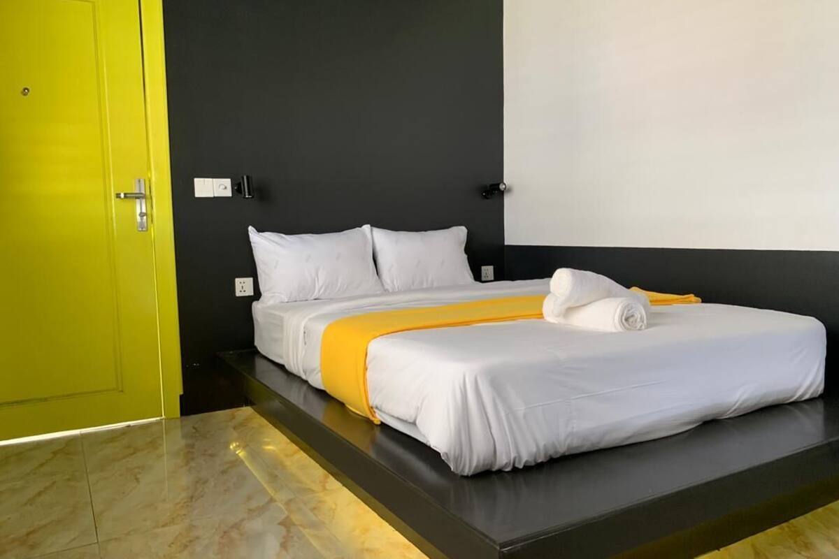 A modern hotel room with a bed, a bright yellow door, and a dark wall.