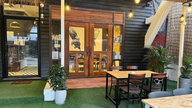 Un espace patio extérieur avec une table et des chaises en bois, une plante en pot et une porte vitrée ornée de panneaux de verre décoratifs.