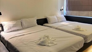 Une chambre d’hôtel avec deux lits, chacun étant équipé de draps blancs et d’une serviette. La chambre dispose également d’un ventilateur de plafond et d’une fenêtre avec un store.