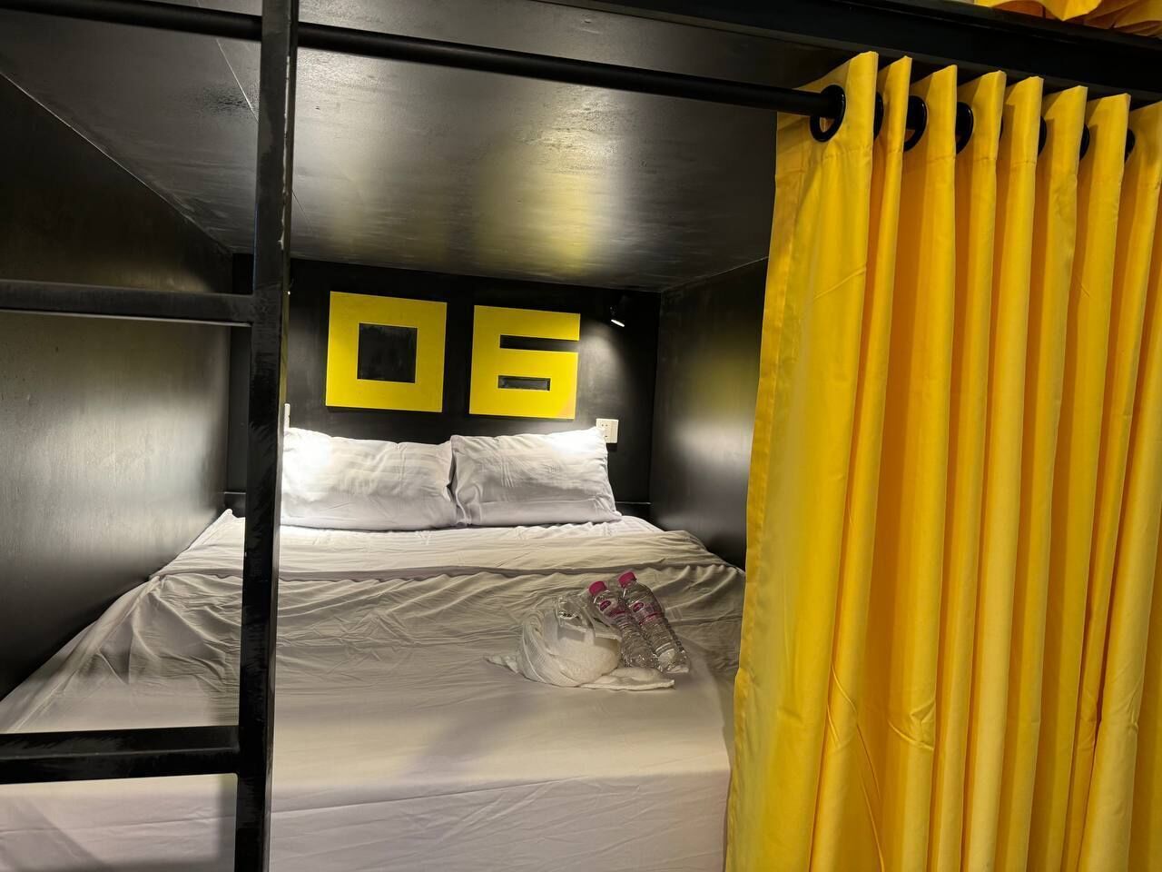 A bunk bed room with a number '06' on the wall, white bedding, and a yellow curtain.