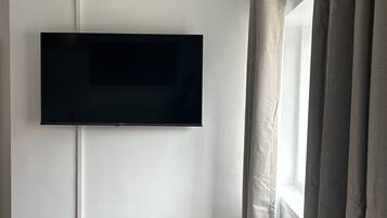 A room with a mounted flat-screen TV on the wall, a window with curtains, and a radiator below the window.