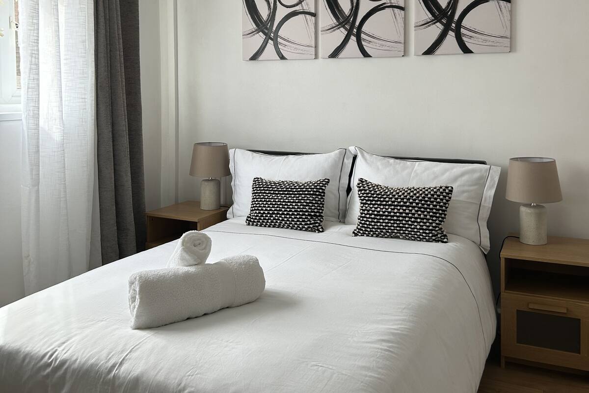 A neatly arranged bedroom with a large bed, two bedside tables, and a wall-mounted abstract art piece.