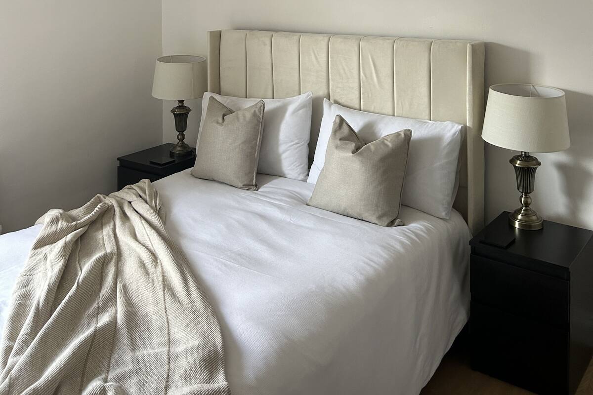 A bedroom with a large bed, two bedside tables, a hanging light fixture, and a wall art piece.