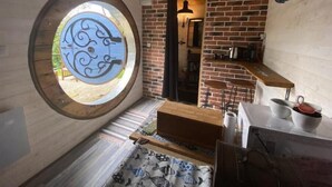A cozy kitchen with a brick wall, a round window, and a wooden ceiling. - The Hobbit du Domaine de la Calotine (Dives-sur-Mer)