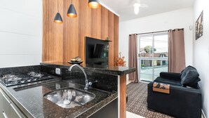 A modern kitchen with a black countertop, a built-in stove, and a sink. There is a black sofa and a TV in the living area.